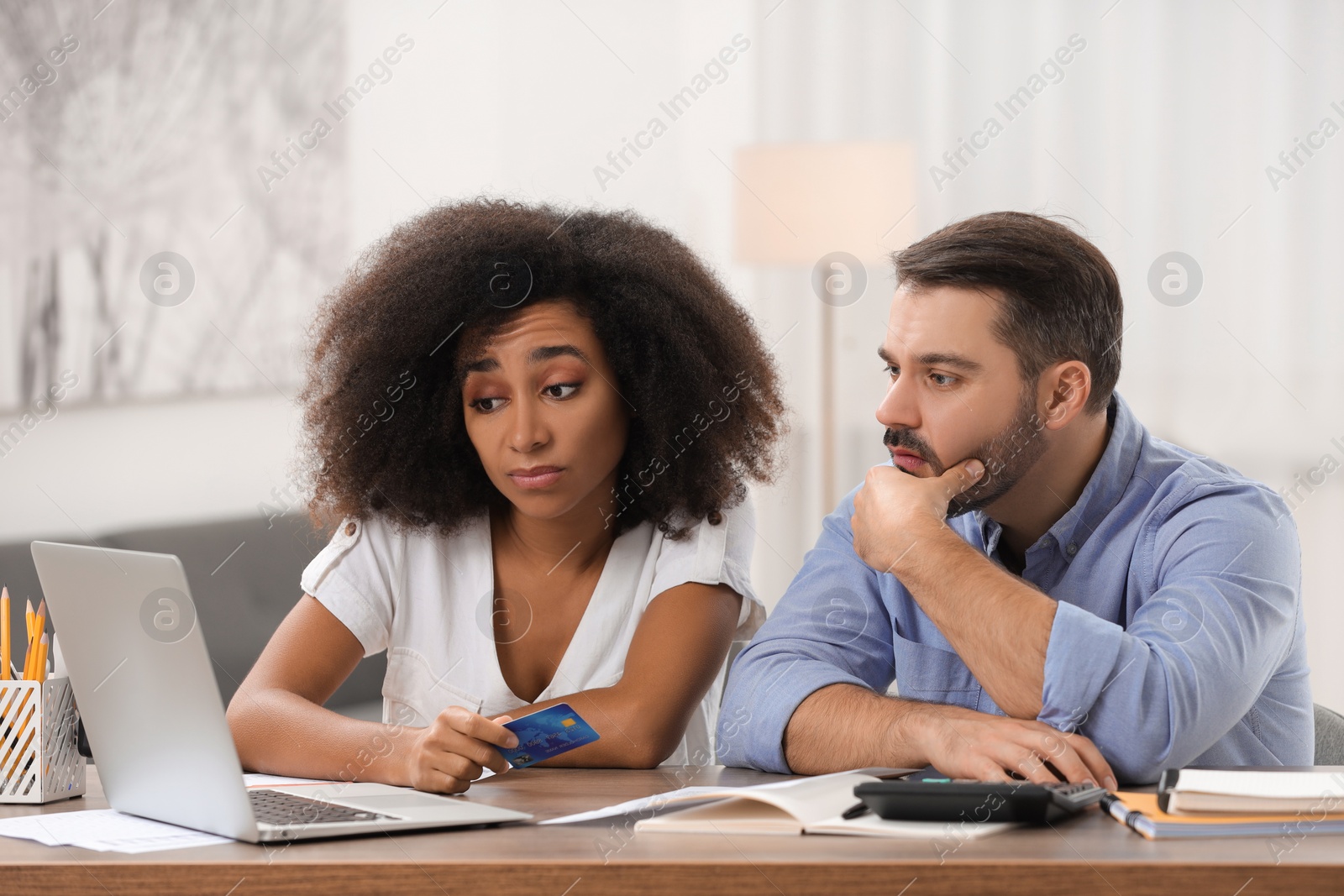 Photo of Confused couple with credit card using laptop for planning budget at home. Debt problem