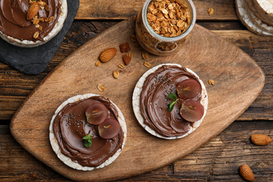 Photo of Puffed rice cakes with chocolate spread and grape on wooden table, flat lay