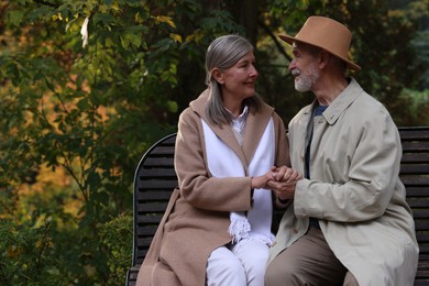 Photo of Affectionate senior couple on wooden bench in autumn park, space for text