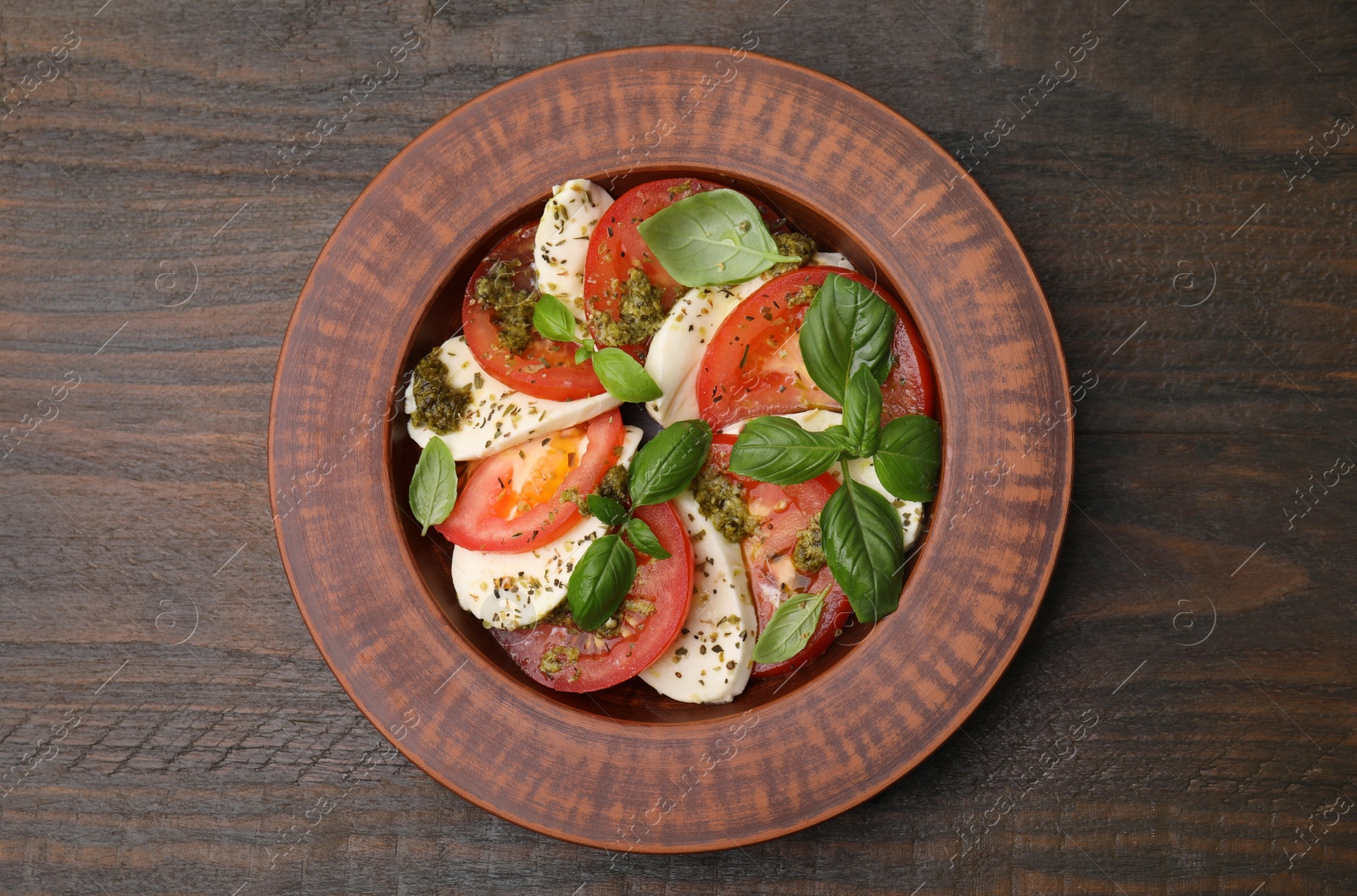 Photo of Plate of delicious Caprese salad with pesto sauce on wooden table, top view