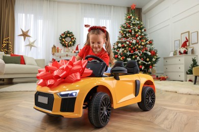 Cute little girl playing with toy car in room decorated for Christmas