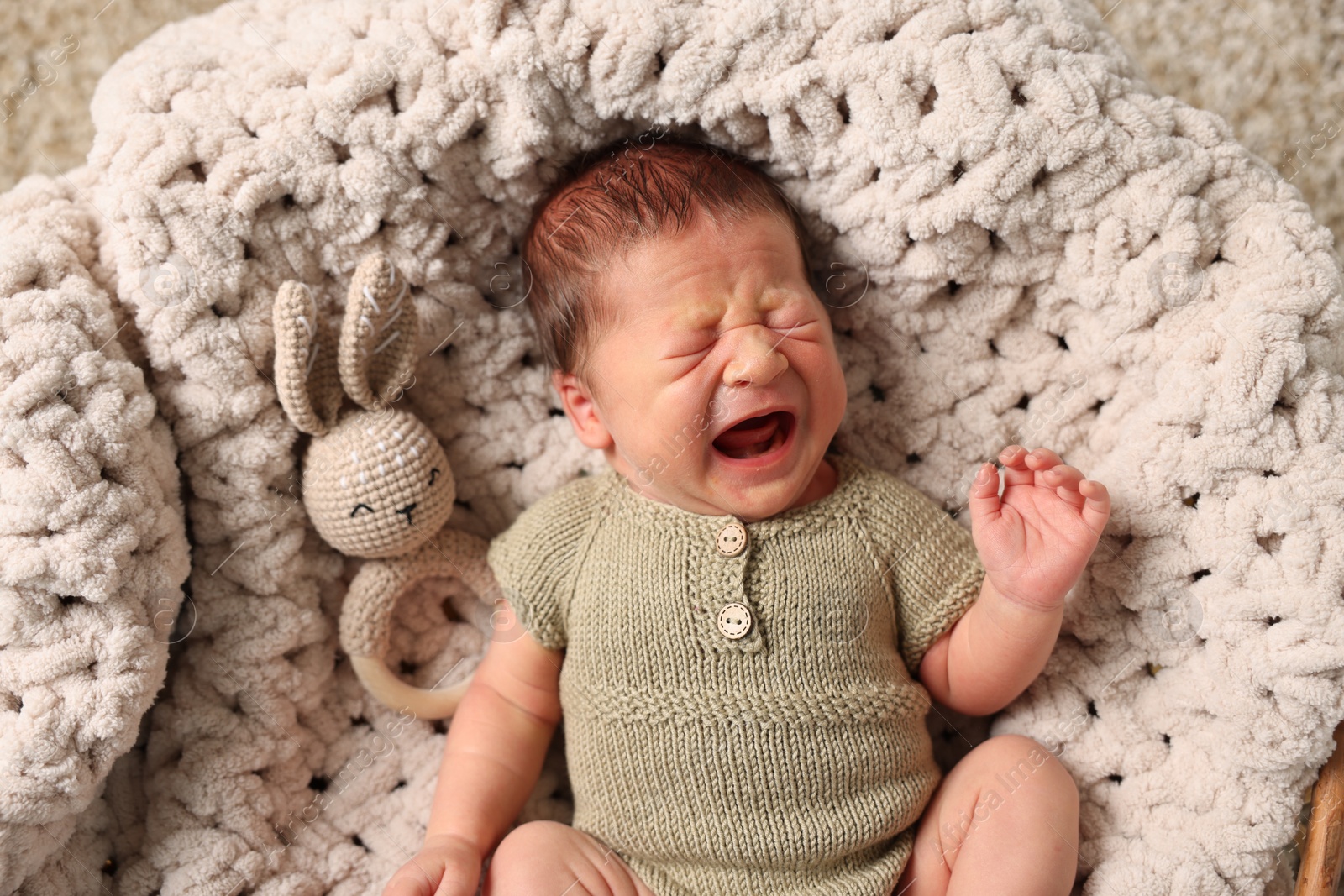 Photo of Adorable newborn baby with toy bunny crying in basket, top view