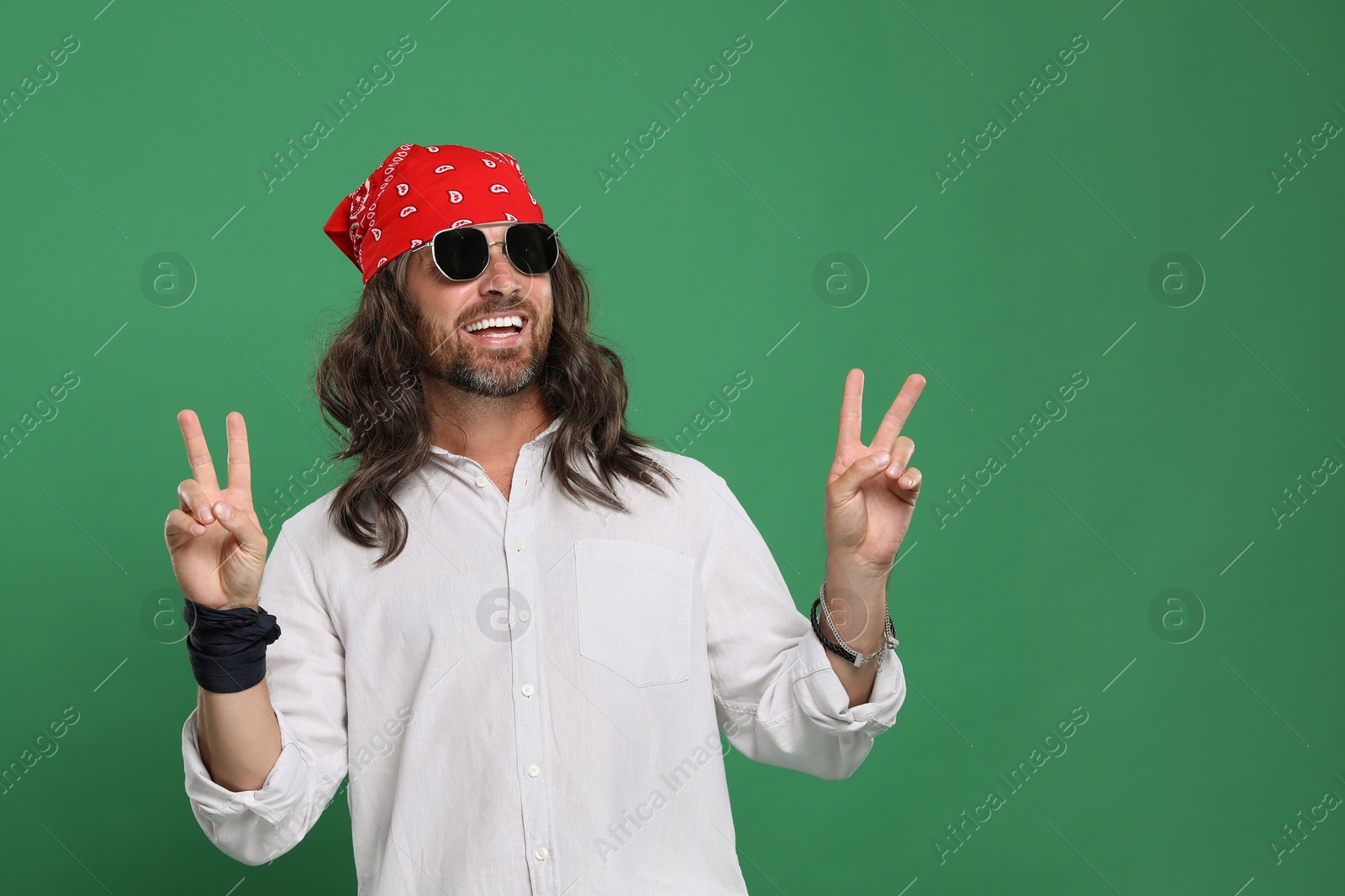 Photo of Stylish hippie man in sunglasses showing V-sign on green background