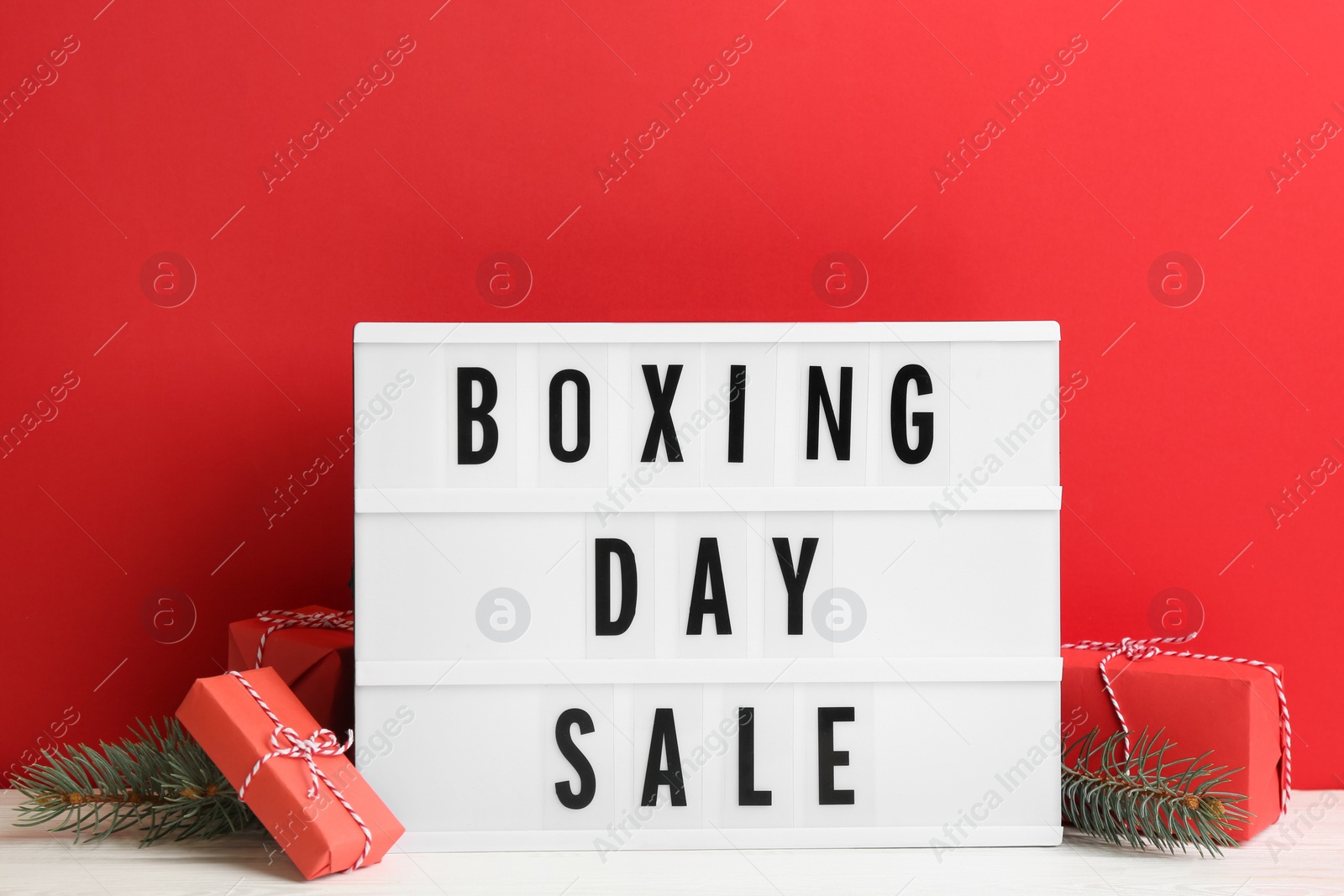 Photo of Composition with Boxing Day Sale sign and Christmas gifts on white table against red background