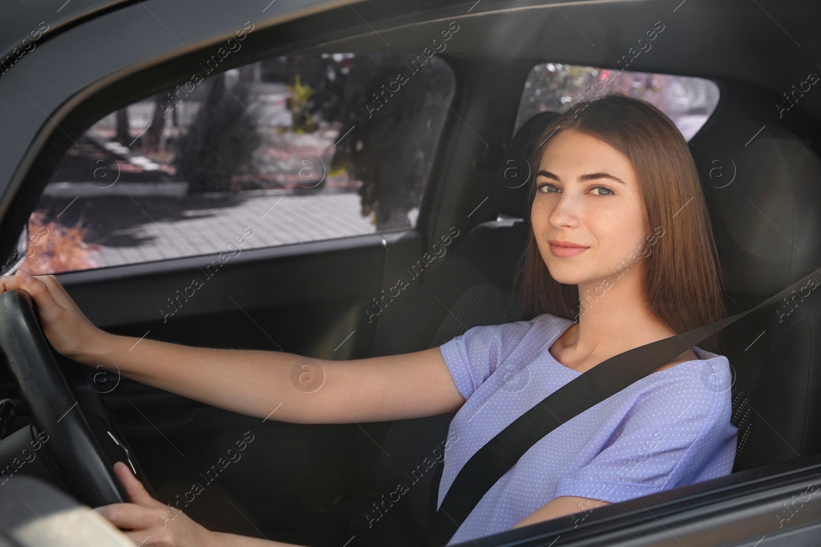 Photo of Young woman with fastened safety belt on driver's seat in car