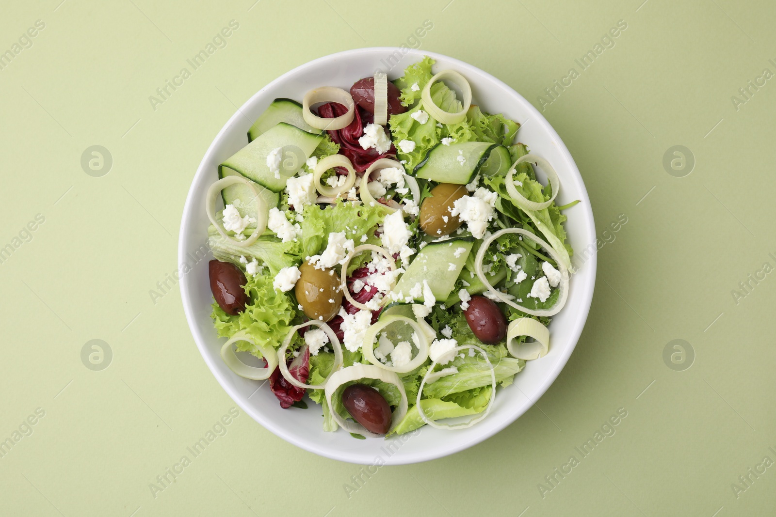 Photo of Bowl of tasty salad with leek, olives and cheese on pale green table, top view