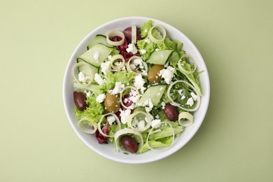 Bowl of tasty salad with leek, olives and cheese on pale green table, top view