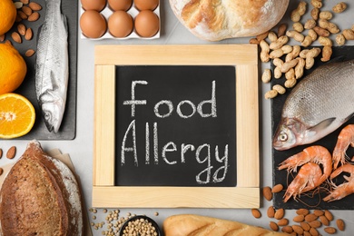 Chalkboard with words FOOD ALLERGY and groceries on grey table, flat lay