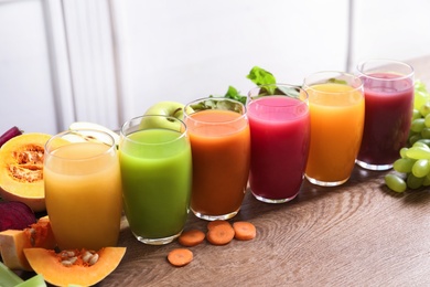 Glasses with different juices and fresh ingredients on wooden table