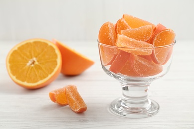 Photo of Tasty orange jelly candies and cut fruit on white wooden table. Space for text