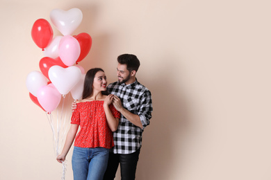 Photo of Beautiful couple with heart shaped balloons on beige background, space for text. Valentine's day celebration