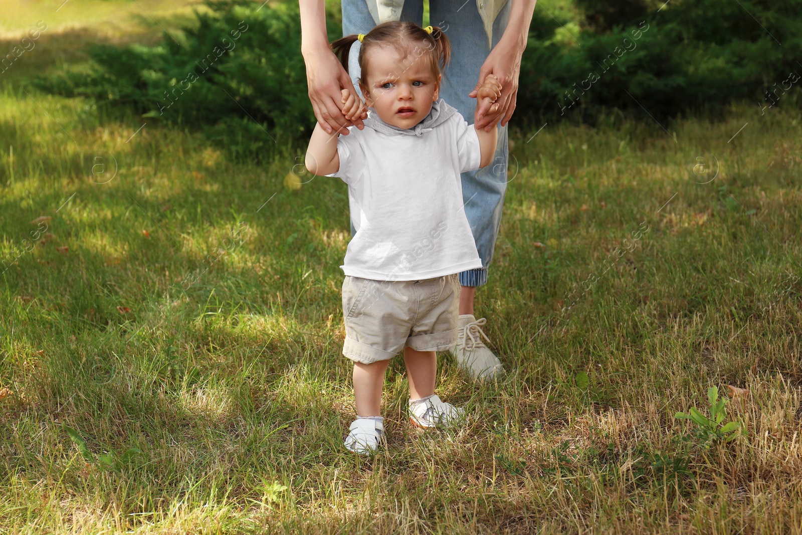 Photo of Mother supporting daughter while she learning to walk outdoors, closeup