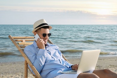 Photo of Happy man with laptop talking by mobile phone on beach. Business trip
