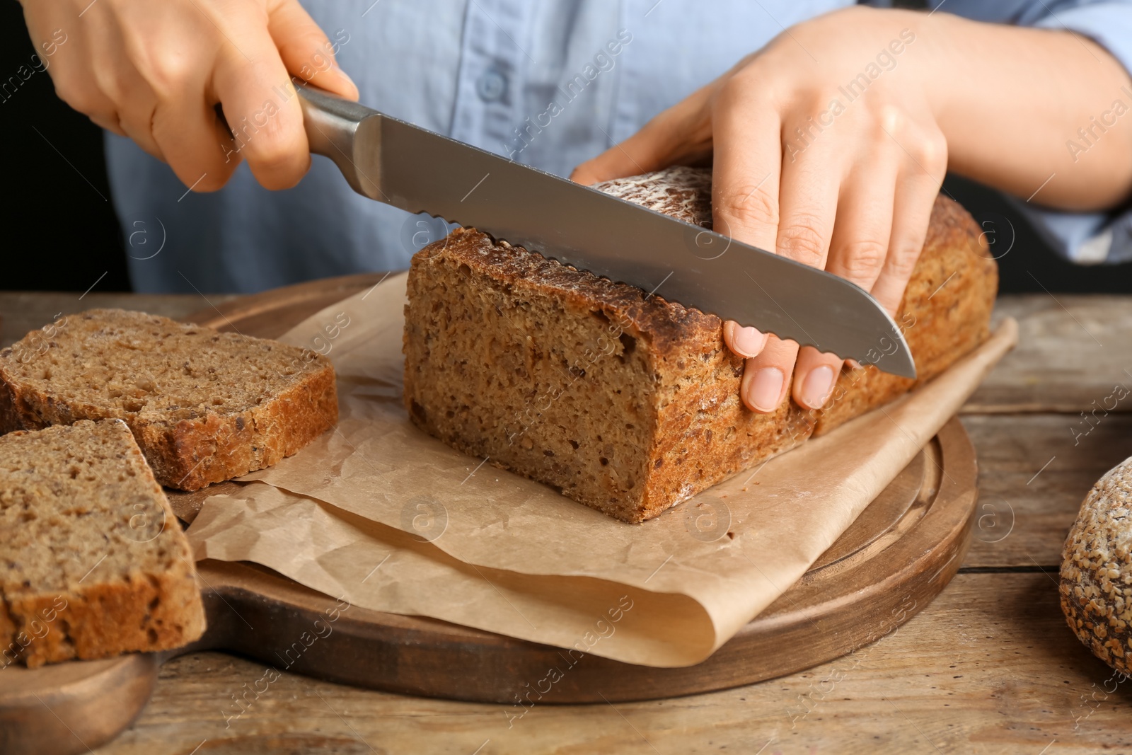 Photo of Woman cutting freshly baked bread at wooden table, closeup