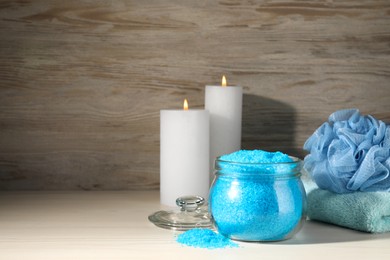 Photo of Aromatic sea salt, burning candles, towel and shower puff on white wooden table, space for text