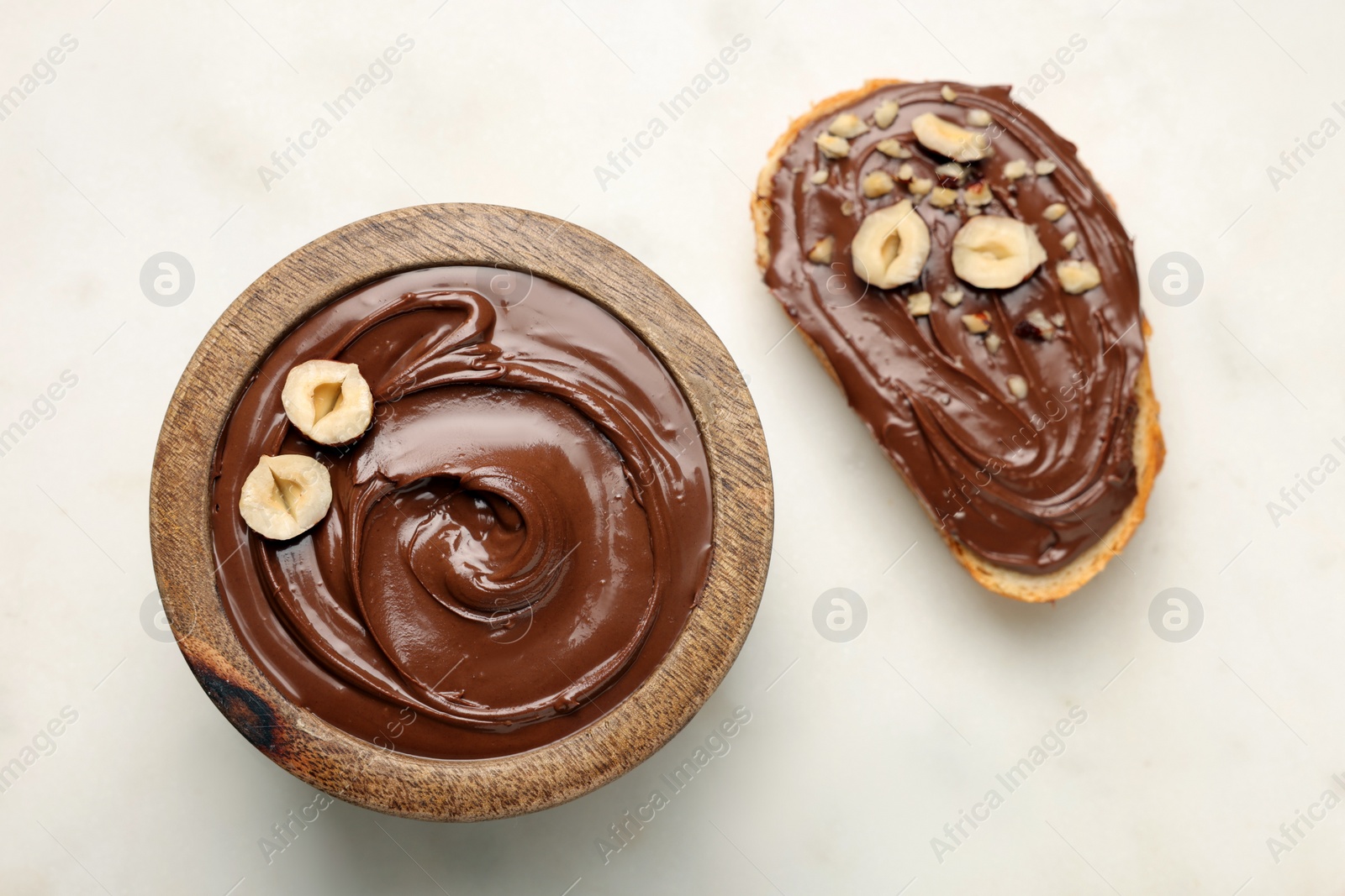 Photo of Bread with chocolate hazelnut spread near bowl on white background, flat lay
