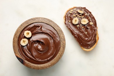 Bread with chocolate hazelnut spread near bowl on white background, flat lay