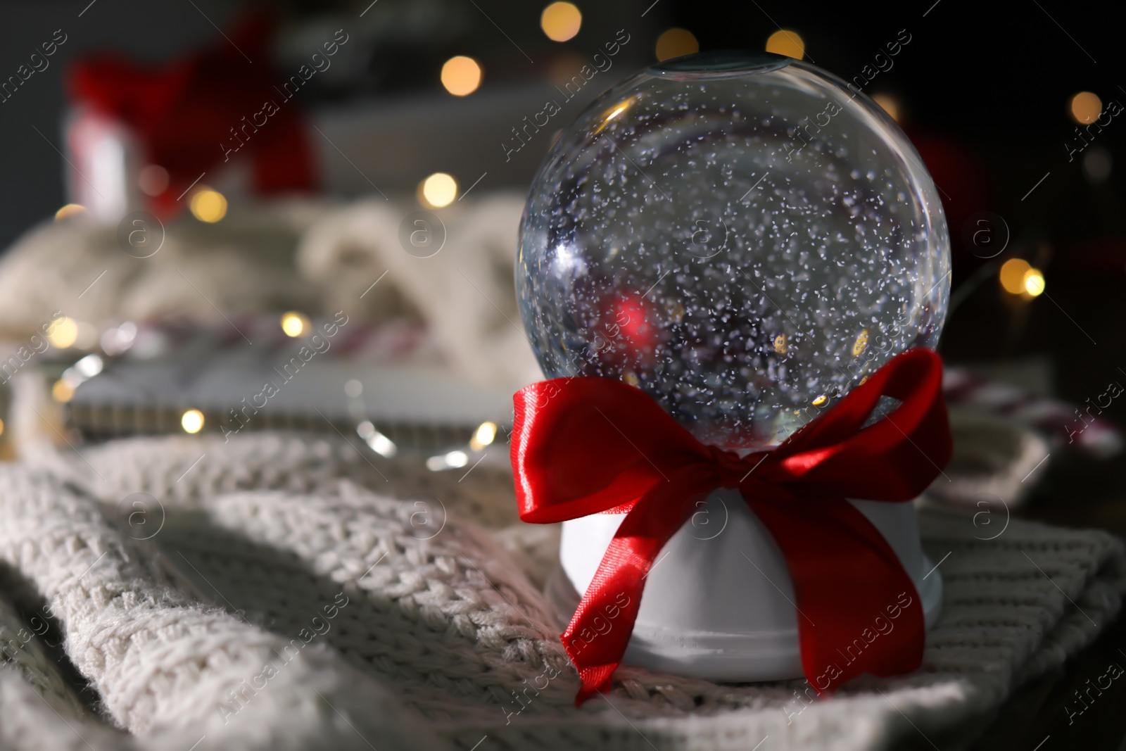 Photo of Christmas snow globe with knitting clothes on blurred background. Space for text