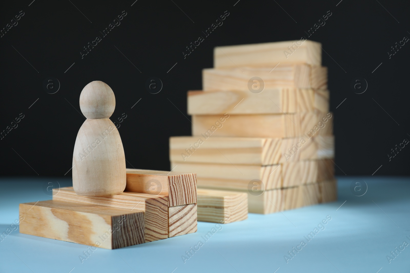 Photo of Stairs of blocks with gap as barrier and wooden human figure on light blue surface, space for text. Path to growth and success