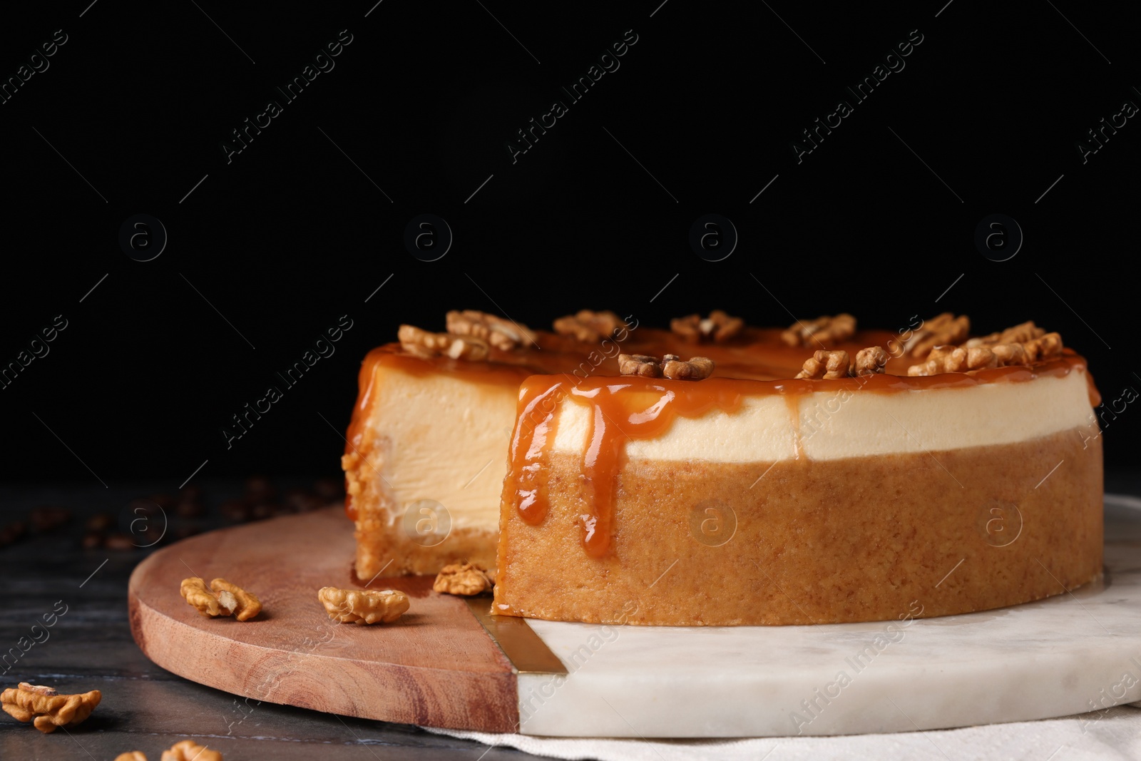 Photo of Delicious cheesecake with caramel and walnuts on black marble table