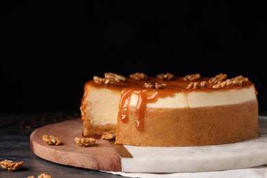 Photo of Delicious cheesecake with caramel and walnuts on black marble table