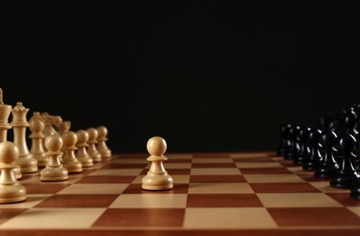 Chess pieces on wooden board against black background