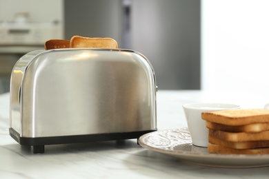Photo of Modern toaster with slices of bread on white table in kitchen