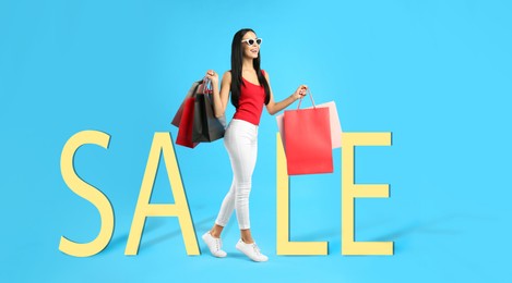 Beautiful young woman with paper shopping bags and word SALE on turquoise background