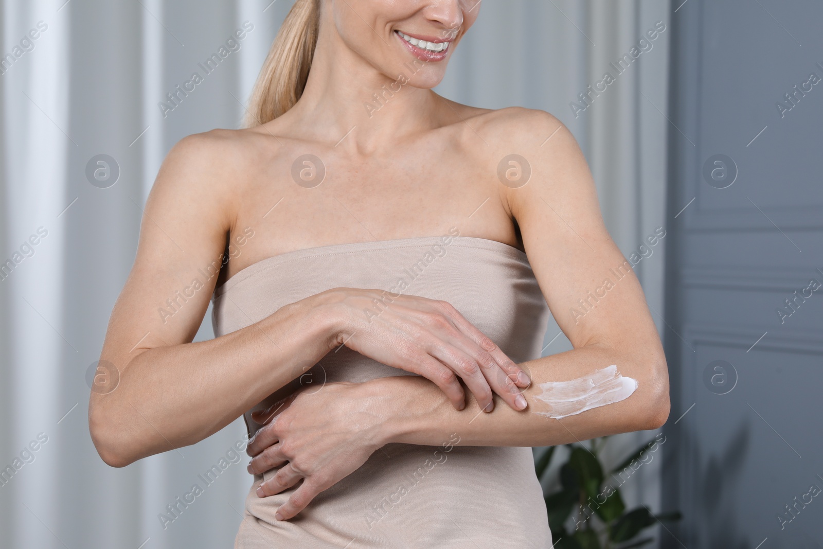 Photo of Woman applying body cream onto arm indoors, closeup