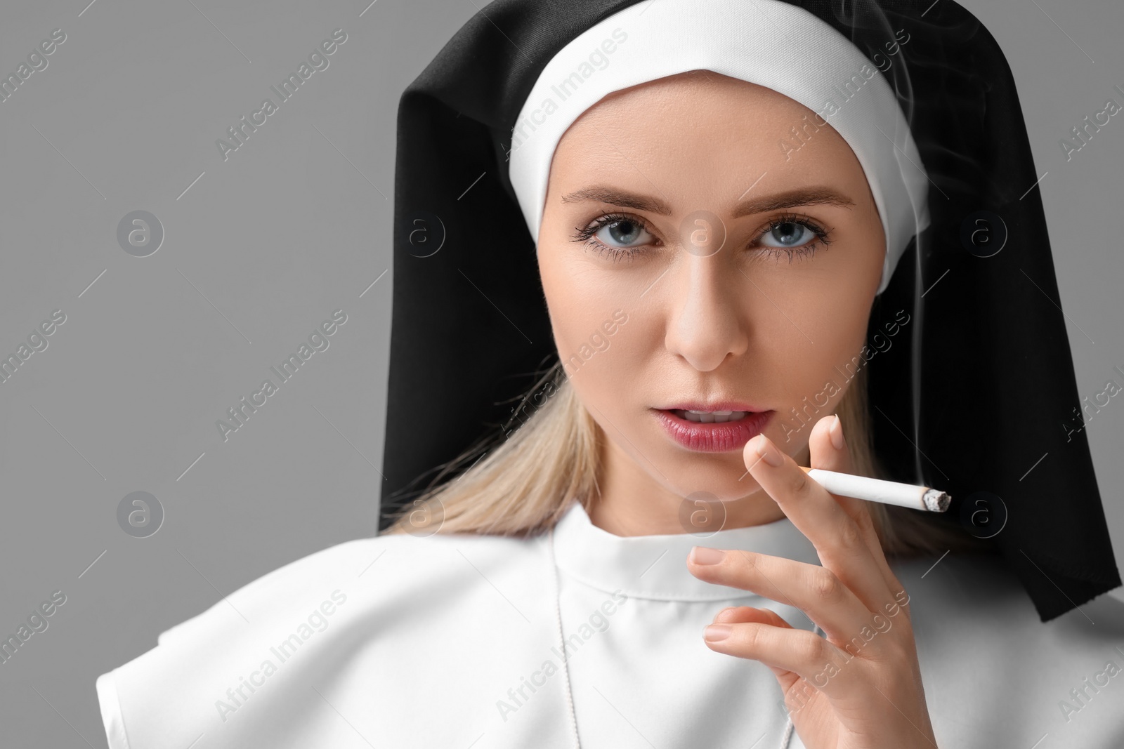 Photo of Woman in nun habit smoking cigarette on grey background. Space for text