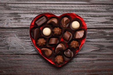 Photo of Heart shaped box with delicious chocolate candies on wooden table, top view