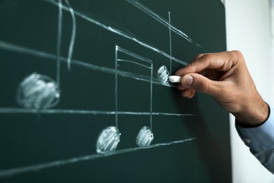 Photo of Teacher writing music notes with chalk on greenboard, closeup