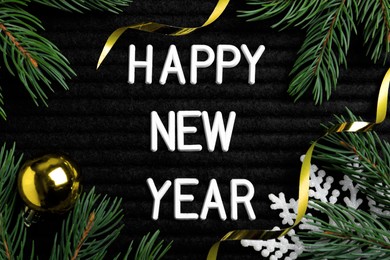 Photo of Happy New Year greeting card. Phrase made with letters and decor on black background, flat lay