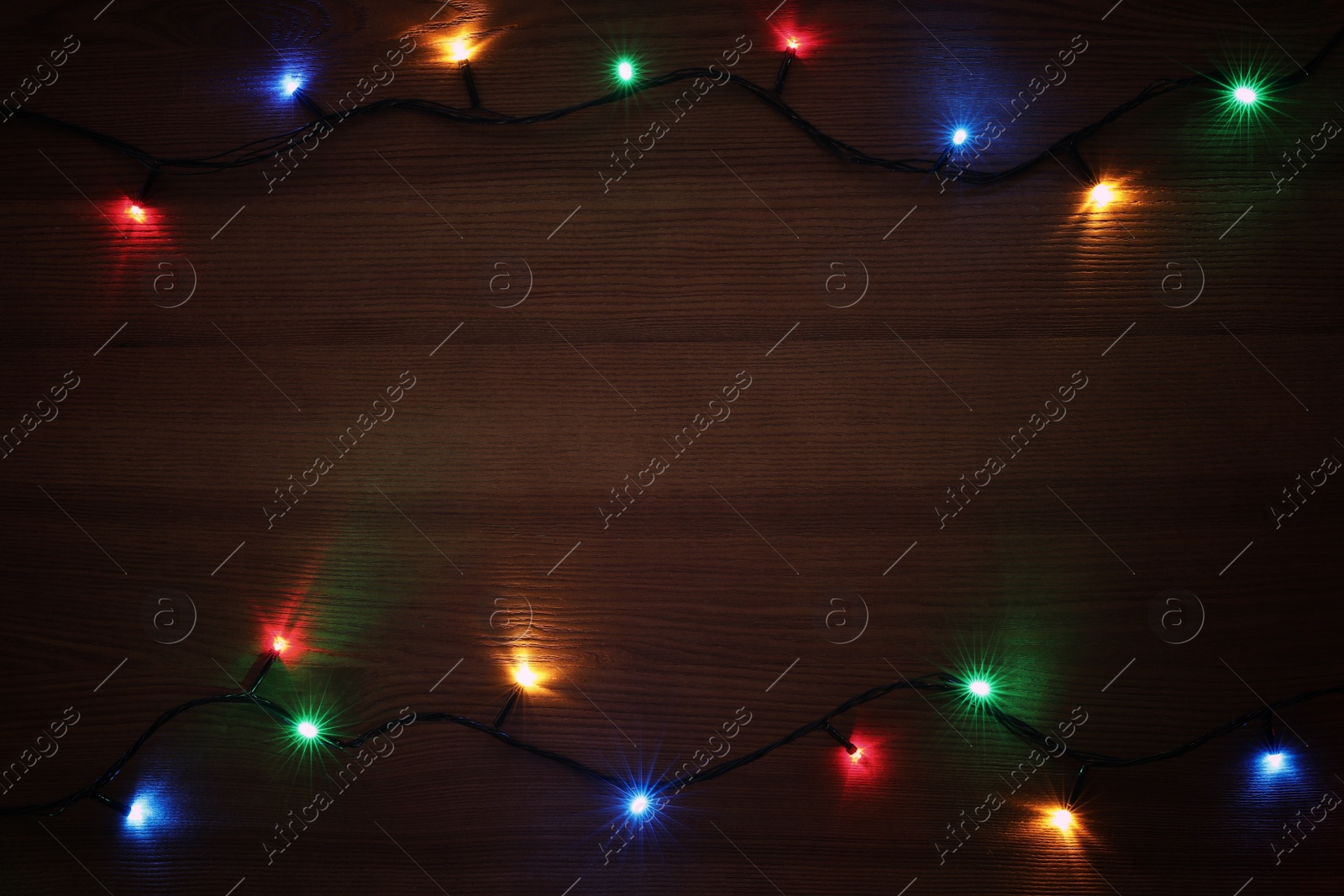 Photo of Frame of colorful Christmas lights on wooden table, top view. Space for text