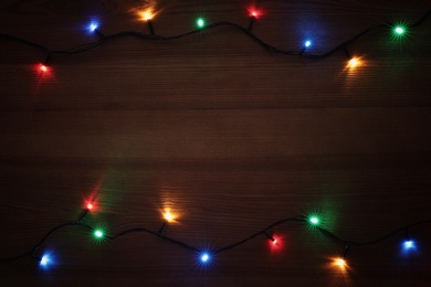 Photo of Frame of colorful Christmas lights on wooden table, top view. Space for text