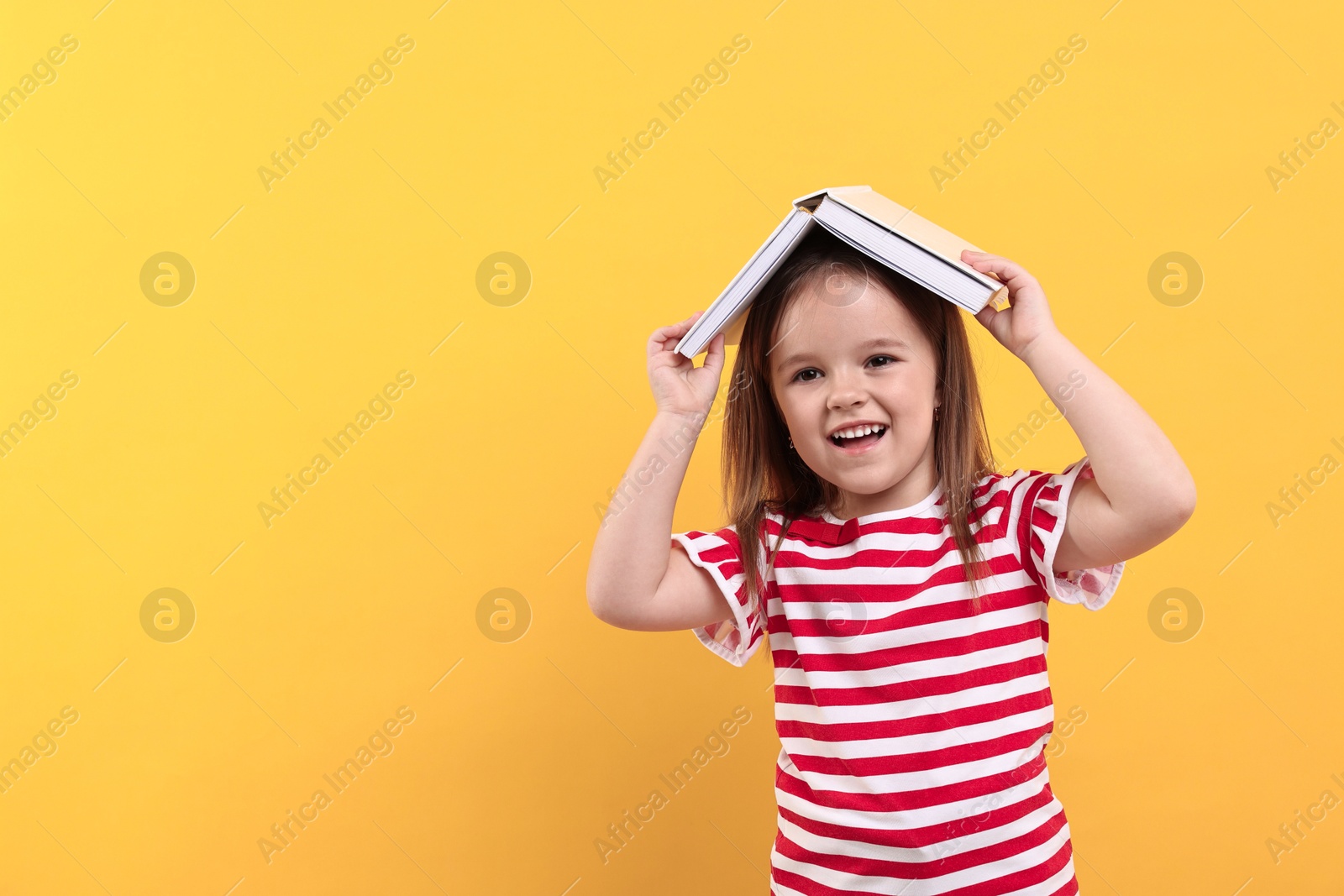 Photo of Cute little girl with open book on orange background. Space for text