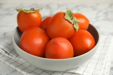Photo of Tasty ripe persimmons in bowl on table, closeup