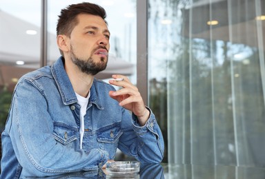 Photo of Handsome man smoking cigarette at table in outdoor cafe