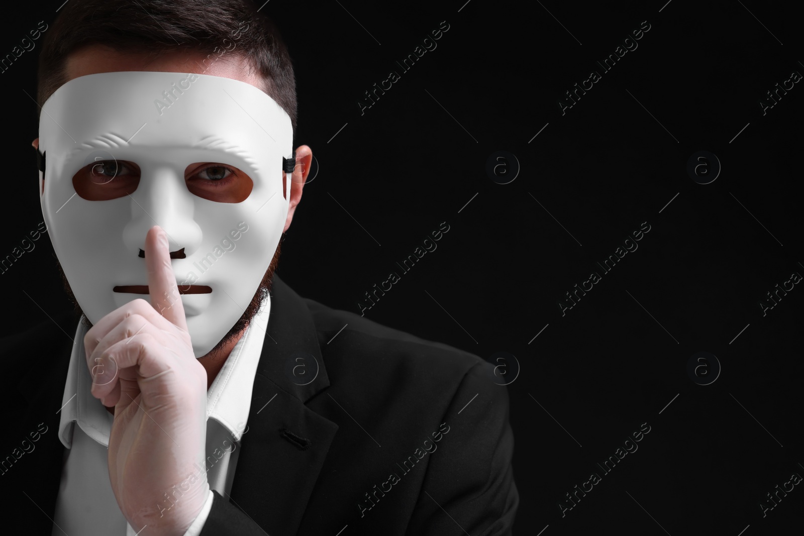 Photo of Man in mask and gloves showing hush gesture against black background. Space for text