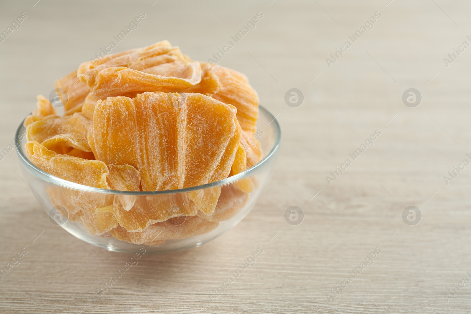 Photo of Delicious dried jackfruit slices in glass bowl on light wooden table, closeup. Space for text
