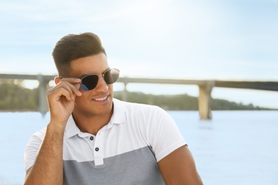 Photo of Handsome man wearing stylish sunglasses near river. Space for text