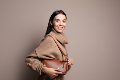 Fashionable young woman with stylish bag on beige background