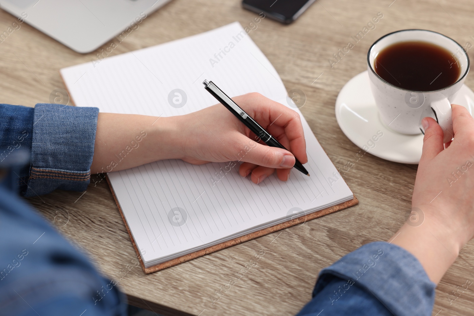 Photo of Young woman writing in notebook at wooden table, closeup