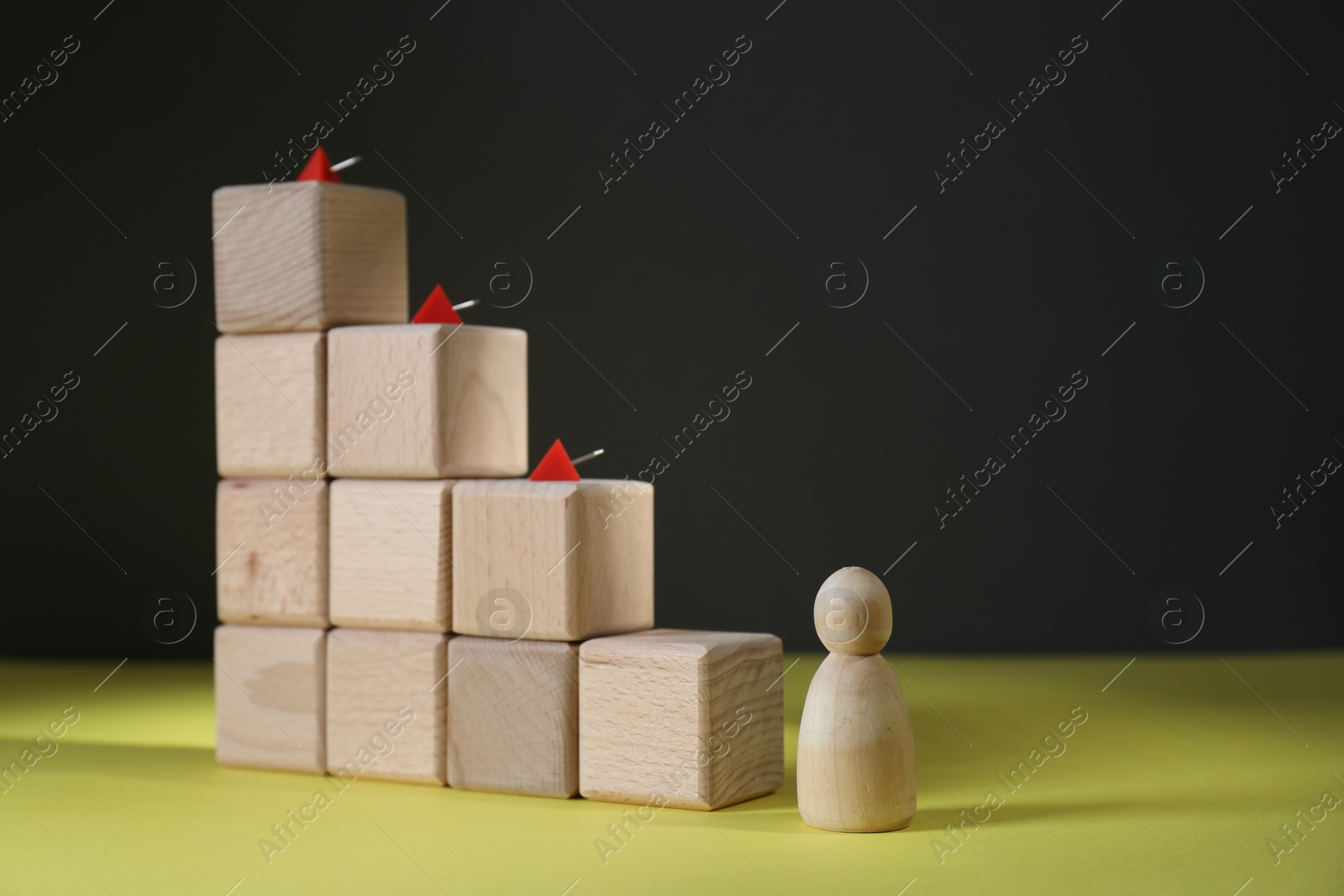 Photo of Stairs of cubes with pins as barrier and wooden human figure on yellow surface, space for text. Path to growth and success