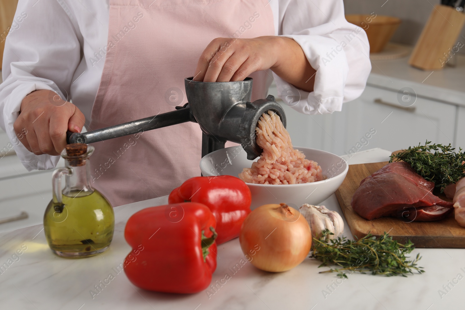 Photo of Woman making chicken mince with metal meat grinder at white table in kitchen, closeup