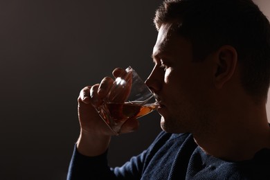 Photo of Addicted man drinking alcohol on dark background, closeup