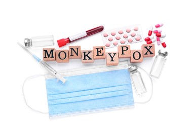 Photo of Word Monkeypox made of wooden cubes, medical face mask, different pills, vials,
syringe and test tube on white background, top view