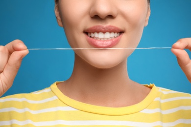 Photo of Young woman flossing her teeth on blue background, closeup. Cosmetic dentistry