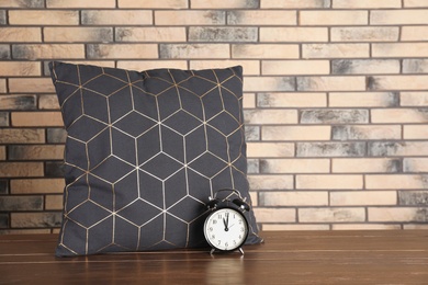 Soft decorative pillow and alarm clock on table against brick wall background