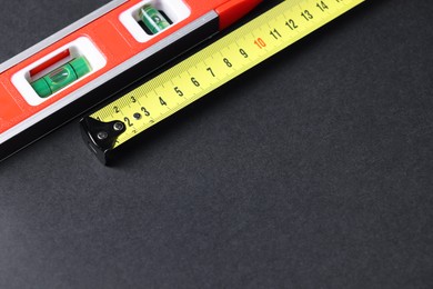 Photo of Building level and tape measure on dark background. Space for text